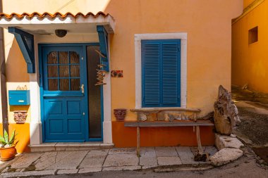 Yellow house with blue door and window with bench in front on old stone made street