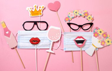 Paper funny girls consisting of sunglasses, wreath, flower crown, lips with a medical mask, a glass of champagne, bottle, heart and a bouquet on the pink background. Quarantine party. Funny fashion.