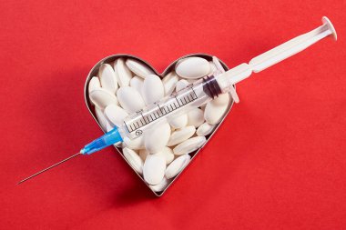 Haplardan yapılmış bir kalp kırmızı zemin üzerinde aşı şırıngasından yapılmış bir okla delinir. yakın plan; makro