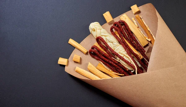 Original edible bouquet consisting of sausages, smoked cheese, spicy cheese, wrapped in craft paper on the black background , top view, copy space.
