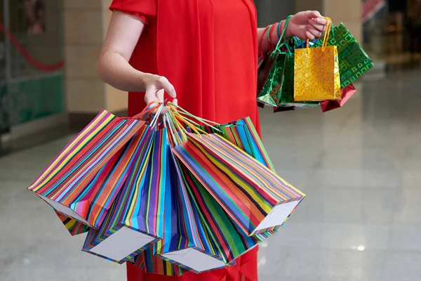 Gift shopping, holidays. Girl's hands with multicolored paper bags at the mall.