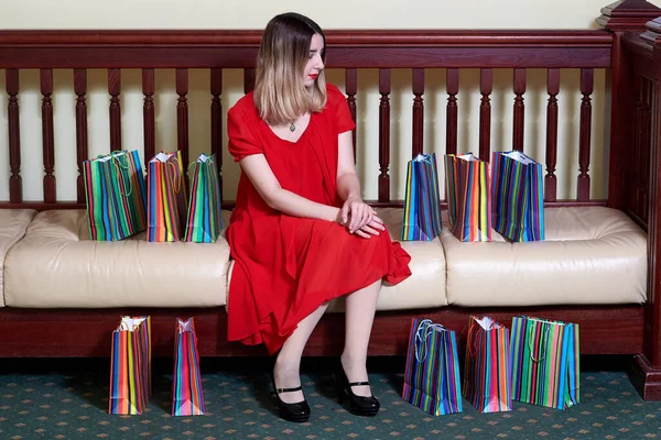 Kız kanepenin üzerinde oturuyor. Etrafı renkli kağıt poşetlerle çevrili..