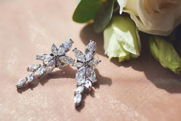 elegant bride's earrings on a veil on the background of a bouquet of flowers. wedding accessories. close-up, macro