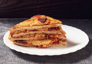 A piece of Italian Pizza Cake with four layers full of grilled salami, ham and moose sausage. Black background, gray canvas napkin.