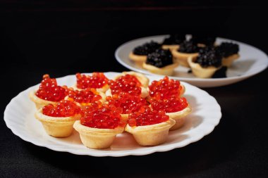 Tartlets full of red and black caviar. Black background, white plates. 