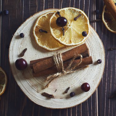 lemon circles, cinnamon sticks, spices, cranberries, cloves on a dark wooden background. square, flat lay