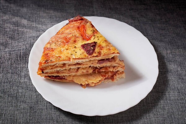 Italian Pizza Cake with four layers full of grilled salami, ham and moose sausage. Black background, grey canvas napkin.