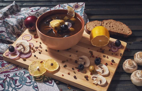 A bowl with vegetarian mushroom solyanka soup, traditional saltwort russian soup. Ceramic bowl on the wooden cutting board.