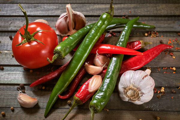 груда красного и зеленого перца чили и помидоры с чесноком гвоздикой на темном деревянном фоне
