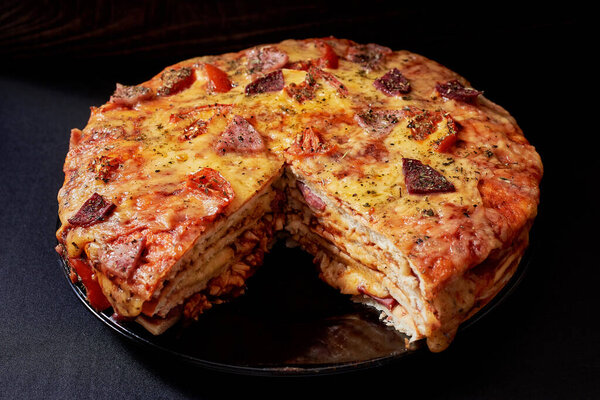 Italian Pizza Cake with four layers full of grilled salami, ham and moose sausage. Black background.