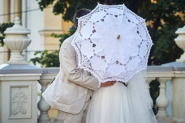 Damat gelini beyaz dantel bir şemsiyeyle öpüyor. Düğün sahnesi balkonda..
