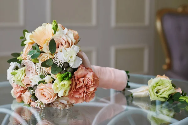 花嫁の花束とピンクのリボンで結ばれた繊細なバラの花の新郎のBoutonniereはホテルの部屋のガラステーブルに横たわっています — ストック写真