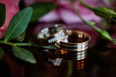 Altın yüzükler ve arka planda güzel bir gül buketi. Detaylar, düğün gelenekleri. Yakın çekim, makro