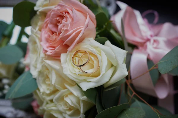 Altın yüzükler ve arka planda güzel bir gül buketi. Detaylar, düğün gelenekleri. Yakın çekim, makro