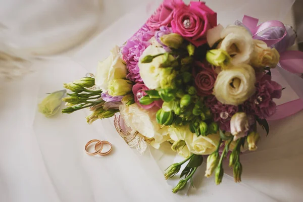 Altın yüzükler ve arka planda güzel bir gül buketi. Detaylar, düğün gelenekleri. Yakın çekim, makro