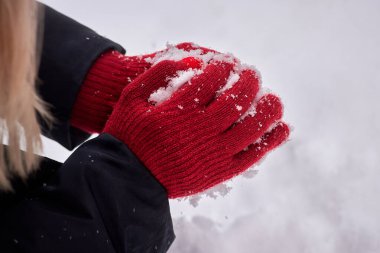 Kırmızı eldivenli eller arka planda bir kartopu oluşturur. Kış eğlencesi, aktiviteler