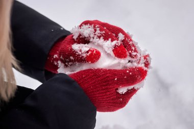 Kırmızı eldivenli eller arka planda bir kartopu oluşturur. Kış eğlencesi, aktiviteler