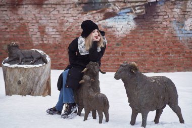Güzel bir genç kız evcil hayvan figürleriyle çevrili bir koyunun heykeline oturur.
