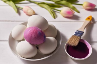 Paskalya kartı. Yumurta, fırça, boya, beyaz bir masada bir buket lale. Yakın çekim, makro