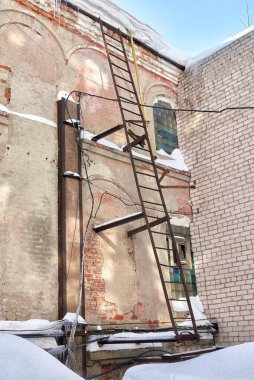 Eski bir sanayi binasının duvarında paslı bir yangın merdiveni. Kış görünümü.