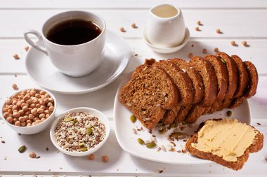 Beyaz tabakta nohut ezmeli tam tahıllı ekmek ve masada bir fincan kahve. Sağlıklı kahvaltı..