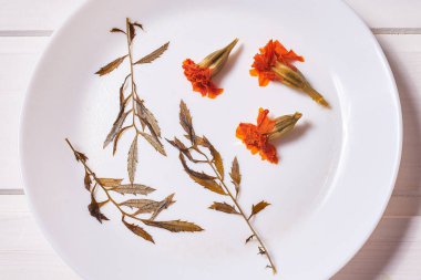 Kurumuş kadife çiçekleri ve beyaz bir tabakta yapraklardan oluşan bir kompozisyon..
