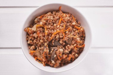 Beyaz ahşap masa üzerinde kızarmış mantar, soğan ve havuçlu karabuğday lapası 