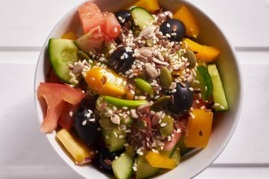 Sebze salatası, zeytinyağlı siyah zeytin, beyaz ahşap zemin üzerine tam tahıl ve tohum serpiştirilmiş. Sağlıklı beslenme.