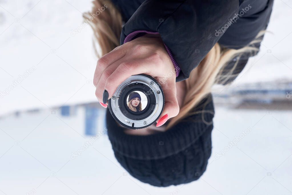A young girl in black clothes holds a photo lens with an inverted image - her face. Close-up.