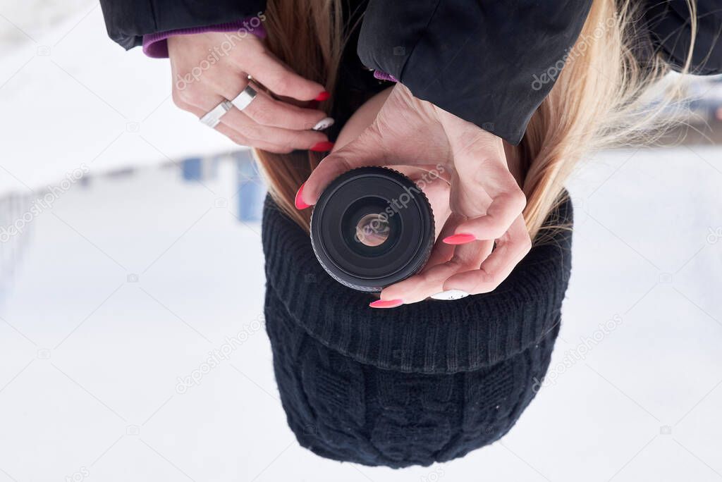 A young girl in black clothes holds a photo lens with an inverted image - her eye. Close-up.