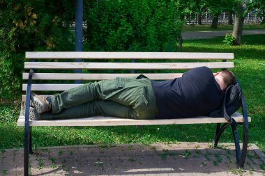 Yorgun bir turist parktaki bankta uyur, başının altına bir sırt çantası koyar. Yakın plan.