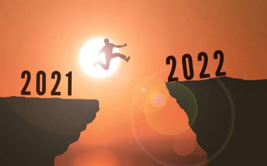 2021 'den 2022' ye Uçurumdan Atlayan Adam. Mutlu yıllar 2022. Günbatımı arka planı Genç adam iki uçurum ya da iki yıllık konsept arasında sıçrıyor