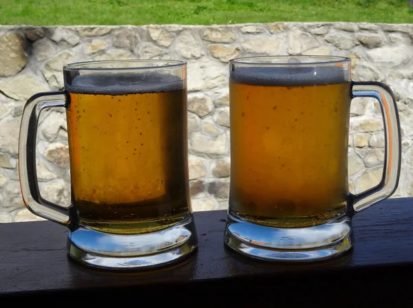 Duas cervejas rascunho na mesa de madeira sobre a parede de pedra velha no fundo — Fotografia de Stock