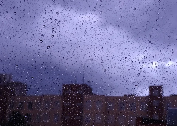 Mira la lluvia en la ciudad a través de la ventana húmeda foto de cristal —  Fotos de Stock