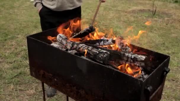 Человек с огненным железом смешивает дрова в гриле барбекю — стоковое видео