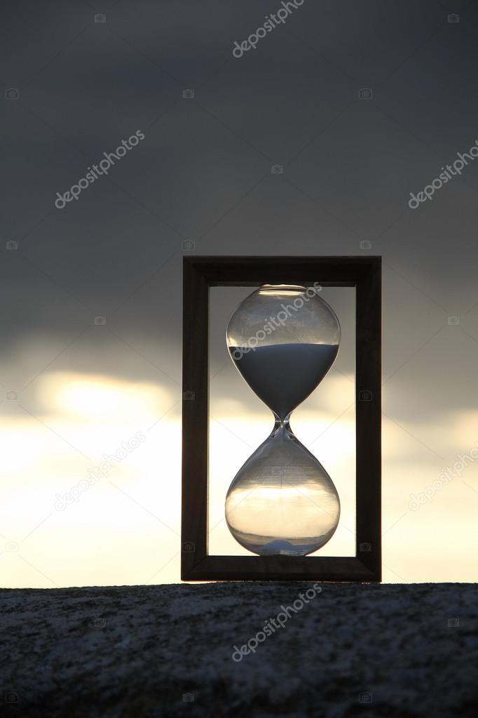 Time glass on concrete parapet over dark sky