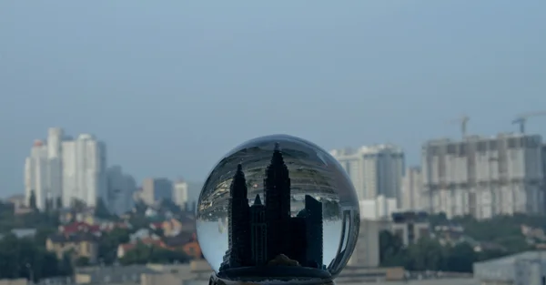 Ciudad de juguete dentro de globo de nieve sobre paisaje real de la ciudad — Foto de Stock