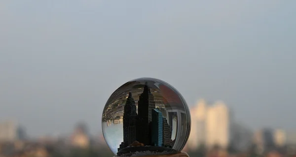 Ciudad de juguete dentro de globo de nieve sobre paisaje real de la ciudad — Foto de Stock