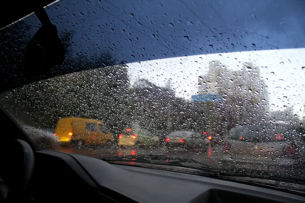 Regardez les gouttes d'eau sur le pare-brise de la voiture de l'intérieur de la voiture à la pluie sur la rue de la ville — Photo