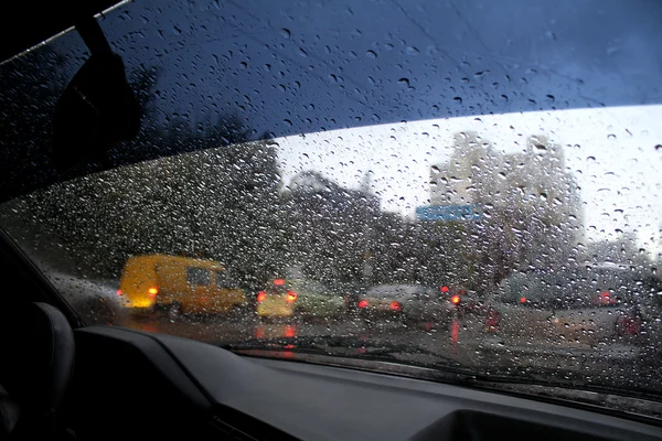 Guarda le gocce d'acqua sul parabrezza dell'auto da dentro l'auto a pioggia sulla strada della città — Foto Stock