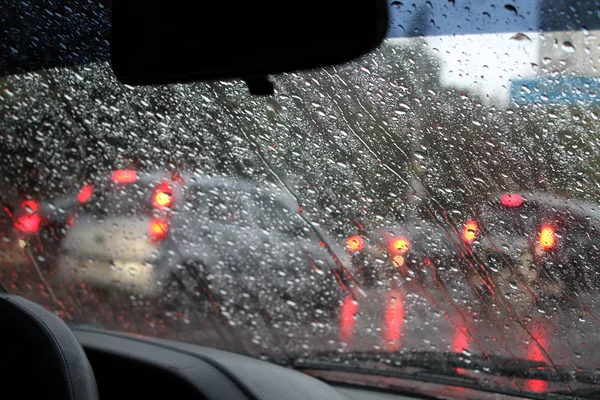 Guarda le gocce d'acqua sul parabrezza dell'auto da dentro l'auto a pioggia sulla strada della città — Foto Stock