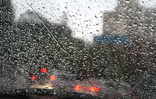 Mira las gotas de agua en el parabrisas del coche desde el interior del coche en la lluvia en la calle de la ciudad — Foto de Stock