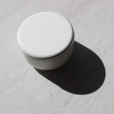 A deep shadow cast by a craft round caddy box standing on a wooden table square stock photo