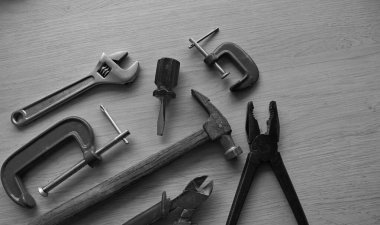 Klasik pense, çekiç, tel kesici, ayarlanabilir ingiliz anahtarı ve kıskaçlar siyah-beyaz bir çalışma masasına yerleştirilmiş.