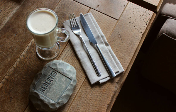 Зарезервированное место за столом ресторана с традиционными столовыми приборами и чашкой молочного кофе