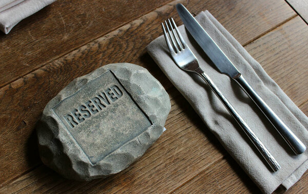 Столовые приборы для одного человека возле знака с надписью, зарезервированной на старом дубовом столе