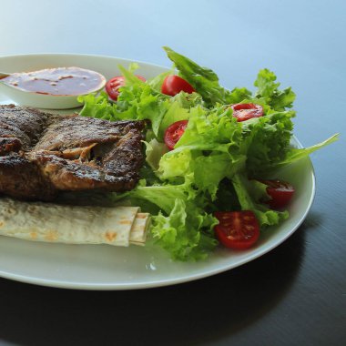 Tabak dolusu yeşil salata, yarım porsiyon domates ve baharatlı biftekli kare fotoğraf.  