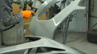 Sprey tabancalı bir uzman, bir araba parçasının boya dükkanında özel astarı olan bir arabadan çıkarıldığını söylüyor.