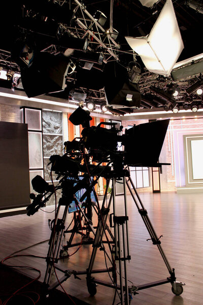 Rail overhead spotlights, heavy duty tripods on wheels, cameras with rigs and view monitors are ready for television broadcast in the studio