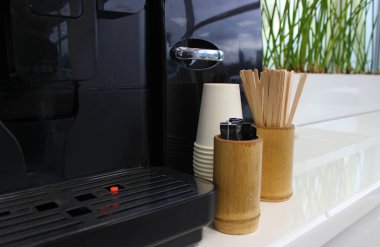 Reception counter with coffee making machine and bamboo coasters for wooden drink sticks and sugar sticks near a column of stacked cardboard cups